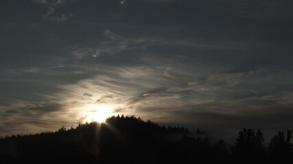 Wall Mural - Dark sky over hill topped with trees becomes day as sun rises on amazing morning filled with fog rolling through and clouds passing by, time lapse.