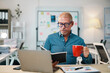 © amnaj - Focused businessman enjoying a cup of coffee while reviewing notes in a modern office