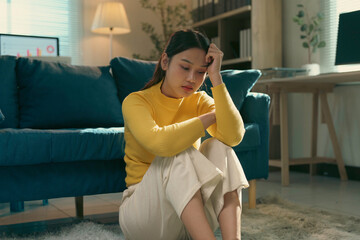 Sad young asian woman sitting on the floor at home, feeling lonely and worried, suffering from emotional problems, mental health concept