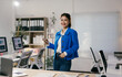 © Parichat - Young asian businesswoman is smiling and holding a smartphone while standing in a modern office with computers and documents on desks