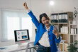 © Parichat - Asian businesswoman is raising her fist in celebration while looking at her smartphone in a modern office, expressing joy and accomplishment in her business endeavors