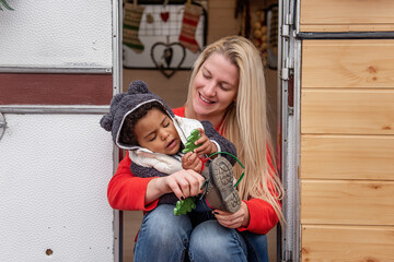 Smiling mother assists her young daughter with his shoe, creating a warm, candid moment at the camper door. Festive decor adds a holiday touch to this outdoor bonding scene.