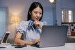 © Parichat - Young asian businesswoman holding a credit card and using laptop for online shopping at her desk in the office at night