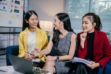 Poster - Three young businesswomen are sitting on a sofa in a modern office, actively discussing business strategies and analyzing data on a laptop, fostering collaboration and teamwork