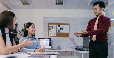 Fototapete - Asian businessman leads a productive meeting with two female colleagues in a modern office, discussing data and charts on a computer screen