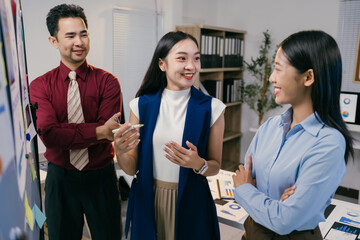 Wall Mural - Three asian businesspeople are discussing a project in front of a whiteboard with charts and graphs, collaborating effectively to achieve success