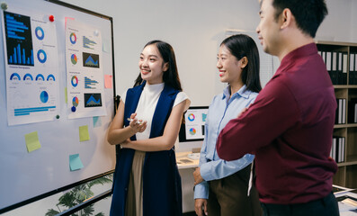 Aufkleber - Three asian businesspeople are discussing charts and graphs on a whiteboard during a productive meeting in a modern office setting, showcasing teamwork and collaboration