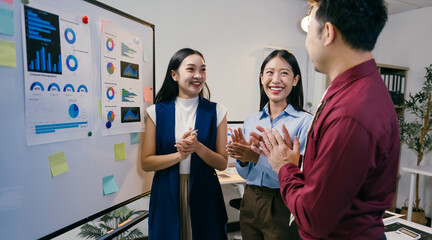 Poster - Asian businesspeople clapping hands, congratulating their colleague after a successful presentation in a modern office meeting room with charts and graphs on a whiteboard