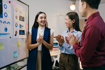 Fototapete - Enthusiastic business team members are clapping, celebrating a successful presentation given by their colleague, standing near a whiteboard with charts and graphs in a modern office environment