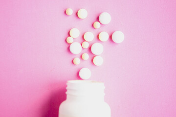 Pills in bottle on pink background, top view