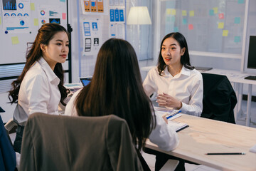 Poster - Three asian businesswomen are actively engaging in a strategic discussion, analyzing charts and reports while collaborating on innovative ideas within a contemporary office setting