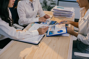 Fototapete - Businesswomen in white shirts are sitting at wooden office desk analyzing financial charts and graphs, collaborating on a project using data visualization