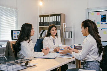 Aufkleber - Three asian businesswomen are sitting at a table in a modern office, collaborating on a project and analyzing charts and graphs