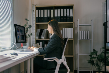 Poster - Young businesswoman sitting at her desk and working on a computer with charts and statistics displayed on the screen, analyzing data and making strategic decisions for her company