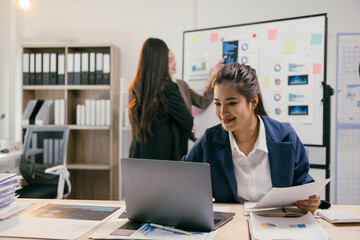 Wall Mural - Smiling businesswoman uses laptop with colleagues discussing charts in office meeting, showcasing teamwork and data analysis