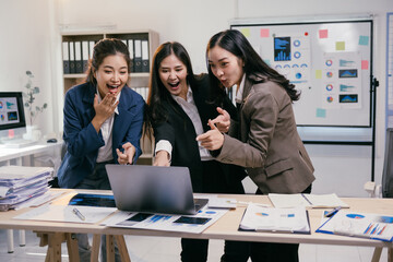 Poster - Three excited asian businesswomen are pointing at a laptop screen, celebrating a successful business achievement in their modern office