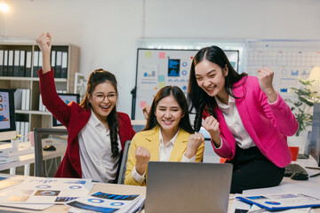 Aufkleber - Three young businesswomen are cheering and raising their fists in the air while looking at a laptop in a modern office, celebrating a successful business achievement together