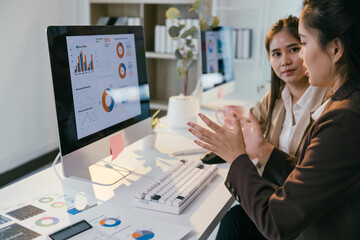 Aufkleber - Two businesswomen are discussing financial charts displayed on a computer screen, analyzing data and collaborating on a project in a modern office environment