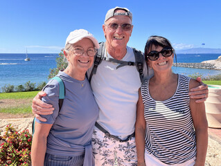 Wall Mural - Group of three seniors smiling people outdoors with sea view on background Enjoying Vacation and Freedom in a sunny day. Happy Retirement Lifestyle Concept