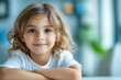 © YouraPechkin - A young child with curly hair smiles while sitting at a table in a bright indoor space