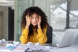 © Liubomir - Young woman in office experiencing stress and frustration. Overwhelmed expression as she sits at desk with crumpled papers, reflecting workplace challenges and pressure. Concept of stress, frustration