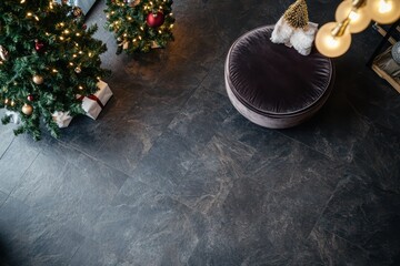 A dark brown stone floor with matte finish, featuring a velvet ottoman, designer lighting, and a festive Christmas tree.