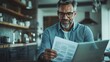 © JoxyAimages - A mature man with glasses reads through documents in a modern kitchen filled with various utensils and decorative elements, exuding focus and contentment.