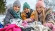 © Anna - Three young women enthusiastically organize a large pile of clothing for donation in a winter landscape, showcasing a spirit of community and giving back
