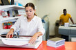 © JackF - Concentrated young woman in white shirt using paper cutter on the table with planners and calculator in the printer house