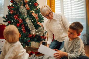 Wall Mural - Grandmother helping grandchildren opening christmas presents