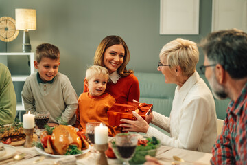 Wall Mural - Family giving christmas present to grandmother at dinner table