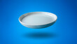 © SaddhaVisual - White ceramic round plate floating or flying isolated on light blue background
