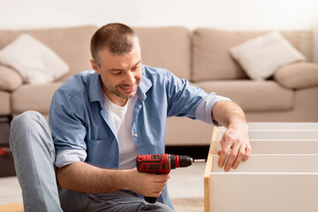 Aufkleber - Man Fixing Furniture Repairing Wooden Cabinet Using Electric Drill Sitting On Floor At Home. Furnishing House