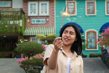 portrait of beautiful happy young asian woman holding sparklers fireworks to celebrate new year eve with garden party standing in outdoor vintage house yard