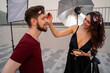 © phoenix021 - Make up on the film set, or photo shoot outdoors, woman makeup artist putting on makeup on male actor. Behind the scenes