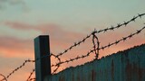 Silhouetted barbed wire fence against a sunset sky.