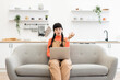 © sofiko14 - Caucasian woman in her 20s working remotely on laptop while sitting on comfortable sofa. She looks focused and engaged in cozy home setting with modern interior design.