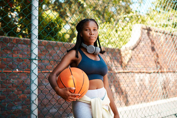 Wall Mural - Black woman, basketball court and fence in portrait with ball as athlete for challenge or exercise. Female person, headphones and coach for competition, match or game for sports or training as player