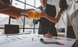 © Phimwilai - Team of business men and women sitting at desks with documents, graphs, charts, holding glasses of champagne, clinking beers, celebrating a party in business success together in the office.