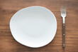 © TATIANA KIM - Empty white plate and fork on wooden background close-up top view.