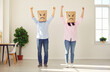 © Studio Romantic - Protest and defiance. Portrait of couple with paper bag over their head displaying drawn angry face. People in casual clothes stand in bright room with their fists raised in protest or displeasure.