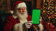 © Valeriia - Santa claus showing green screen tablet sitting near christmas tree