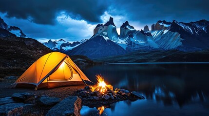 Wall Mural - camping tent by the lake with mountains, glowing fire under stormy sky.