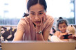 © Westend61 - Woman working on laptop with daughter in background at home