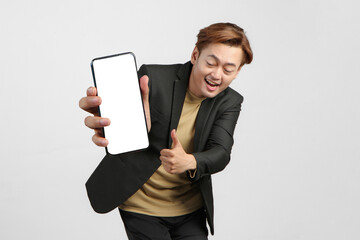 portrait of happy asian businessman wearing suit holding mobile phone and showing blank screen  giving thumb up gesture on isolated background.