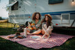 © Halfpoint - Couple sitting by caravan, enjoying peaceful moment. Man playing guitar and singing song to his girlfriend. Camping trip for young people.