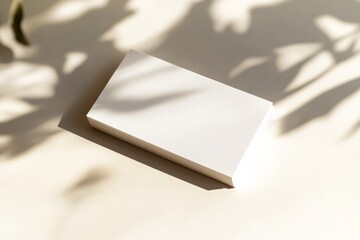 Fototapete - A neatly stacked set of white business cards illuminated by soft sunlight, casting long shadows that create a warm and inviting atmosphere.
