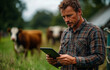 © Vadim - Farmer uses tablet while managing cattle. A farmer in a checkered shirt uses a tablet to monitor his cattle on a green farm during daylight hours.
