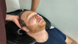 © fotoworld - A man with red hair enjoys a relaxing hair wash at a salon, illustrating self-care and grooming concepts
