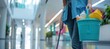 © Eyepain - cleaning woman is standing inside a office building holding a bucket fulfilled with chemicals and facilities copy space
